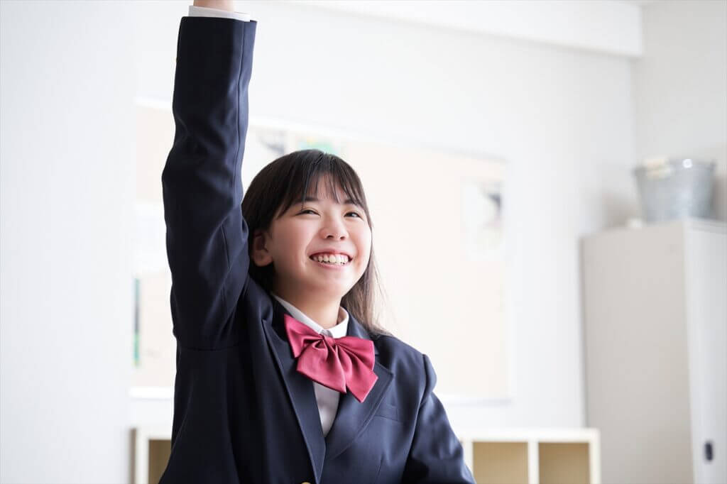 手を挙げる笑顔の女子中学生の画像